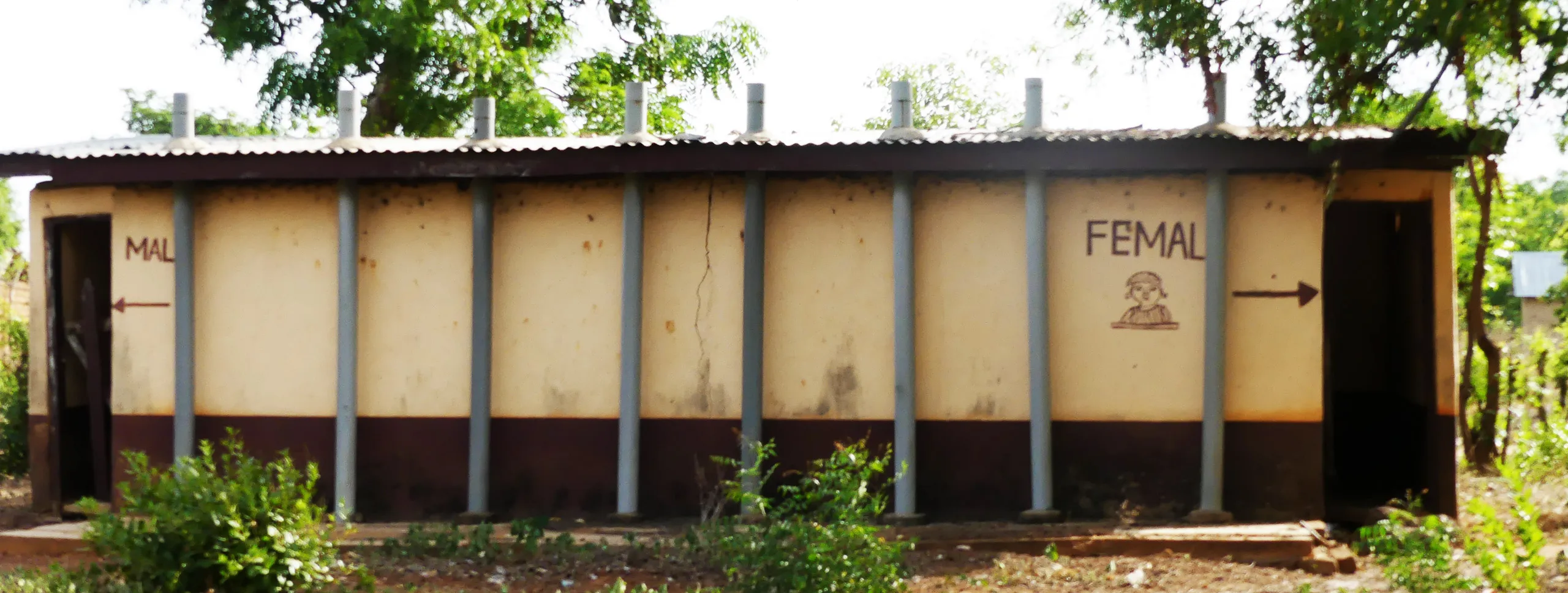 Exterior view of a public latrine building with painted signs indicating separate male and female entrances.