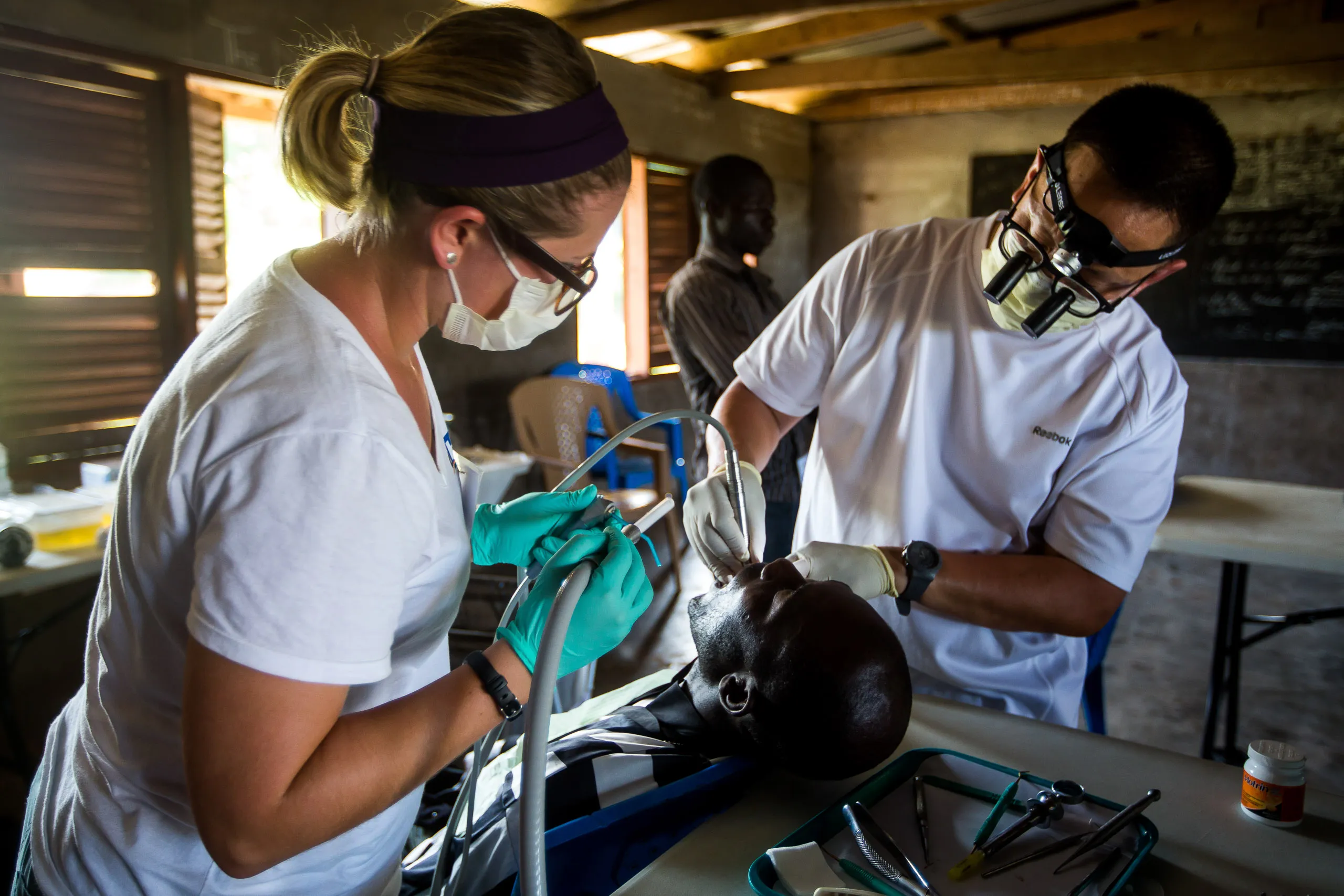 A medical team provides dental care to a patient, with a female dentist using suction and a male dentist performing an examination.